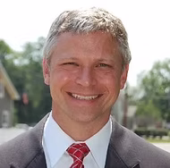 Professional headshot of smiling businessman in suit and red tie