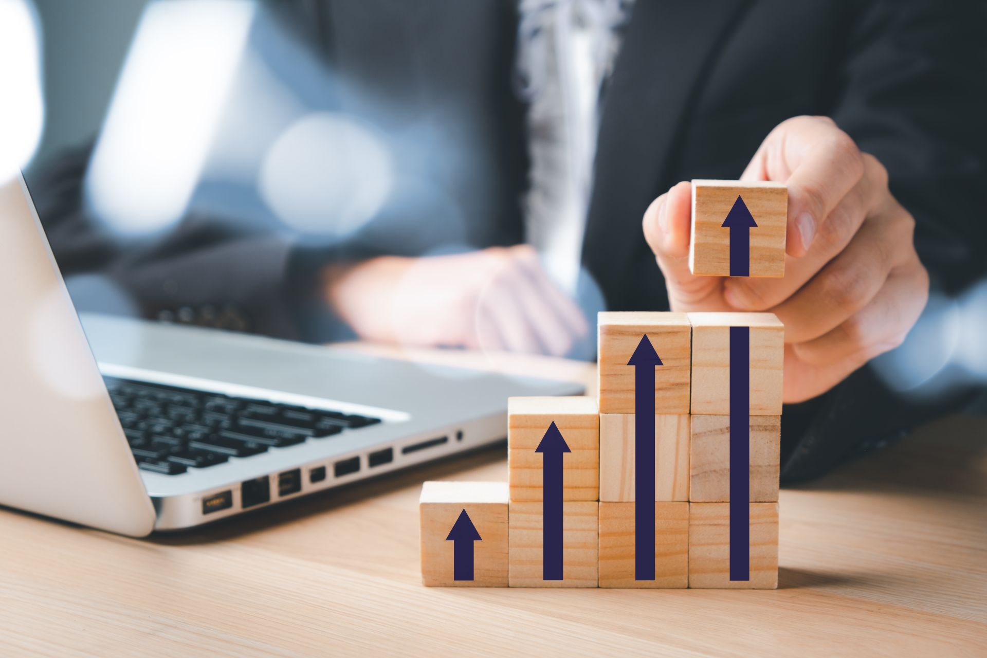 Hand stacking wooden blocks marked with upward arrows beside a laptop