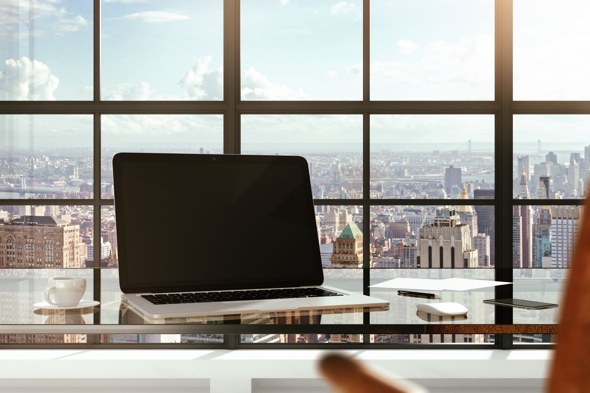 Laptop on a desk in front of floor-to-ceiling windows overlooking a city