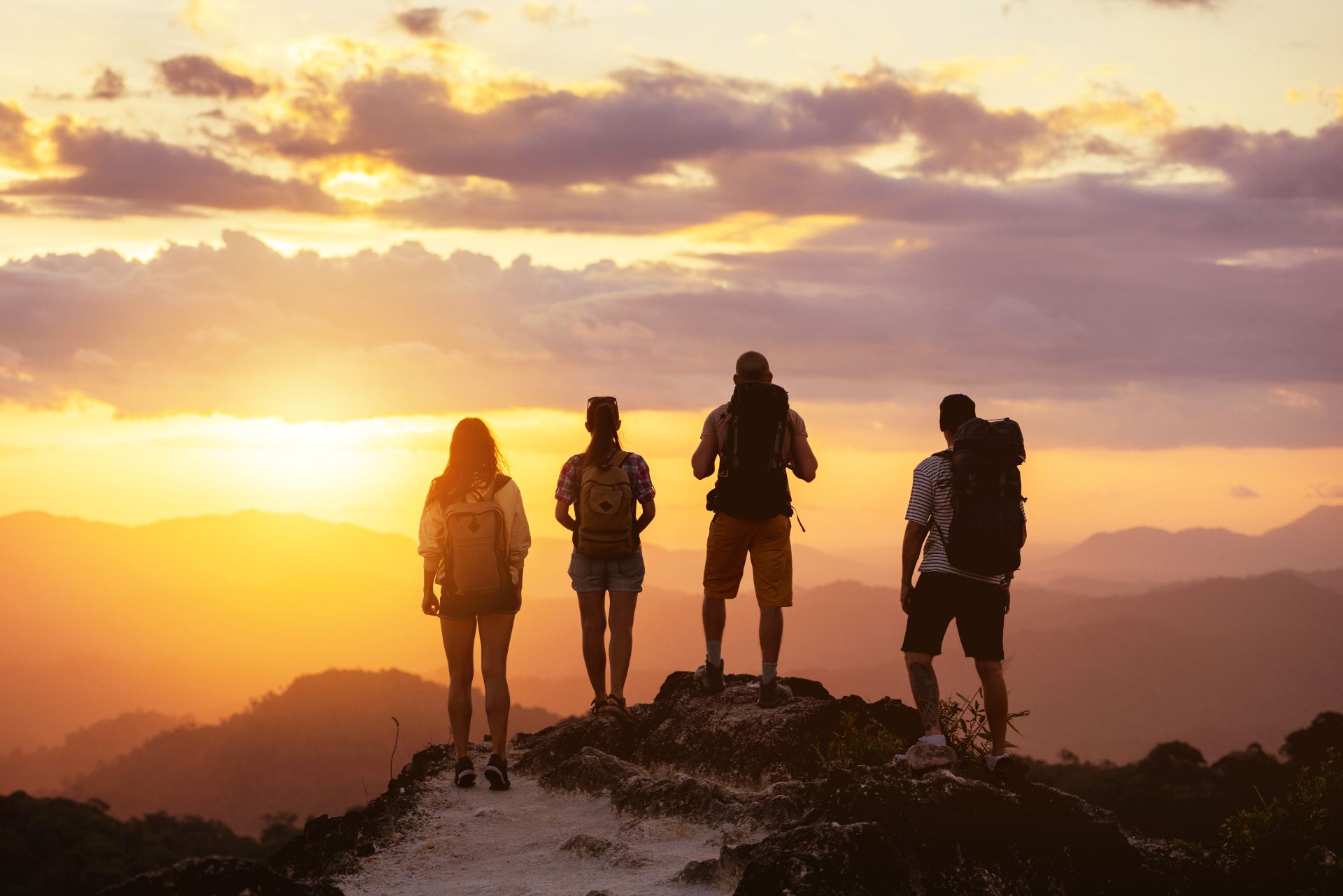 Four hikers standing on a mountain summit at sunset