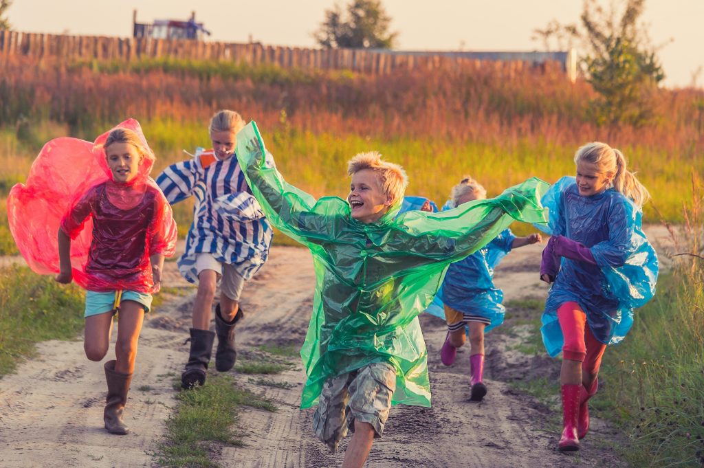 Children in raincoats running together through a field